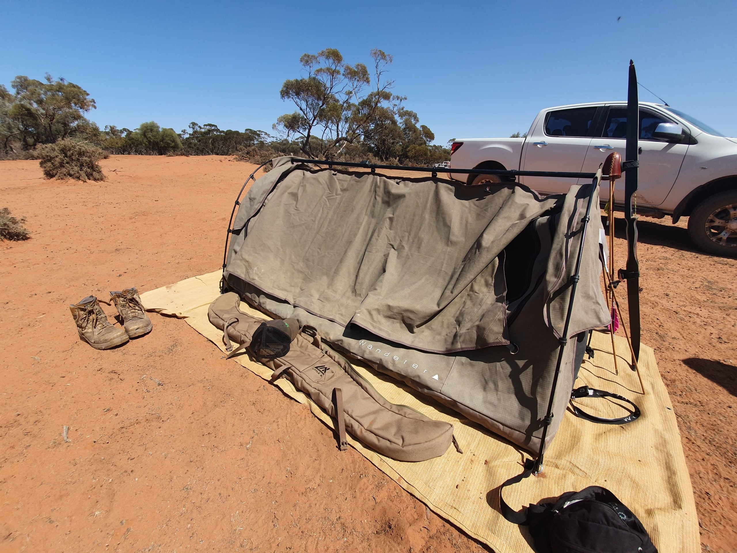 Swag camp in red dirt country, a recurve bow resting on the ute and a Little Ax case on the mat