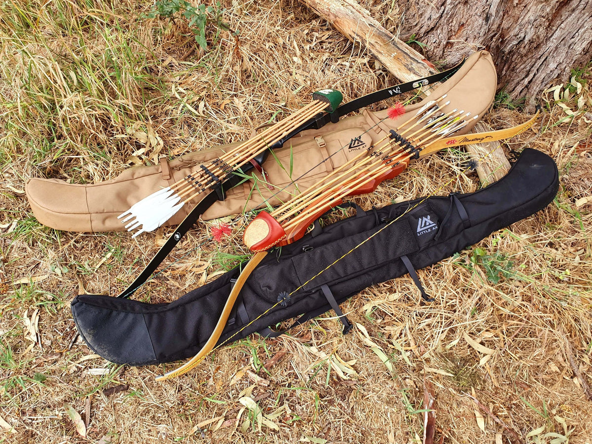 Two Little Ax bow cases in coyote brown and black on dry grass with a recurve bow, wooden arrows and a quiver